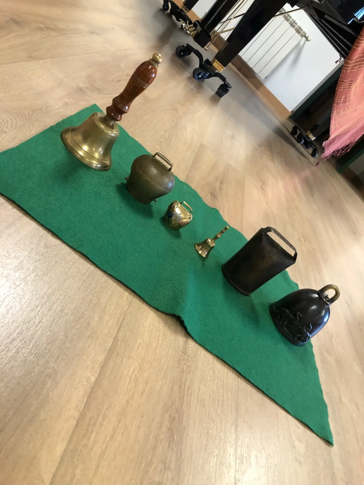 Cinco campanas de distintos tamaños alineadas sobre un fieltro verde en el aula