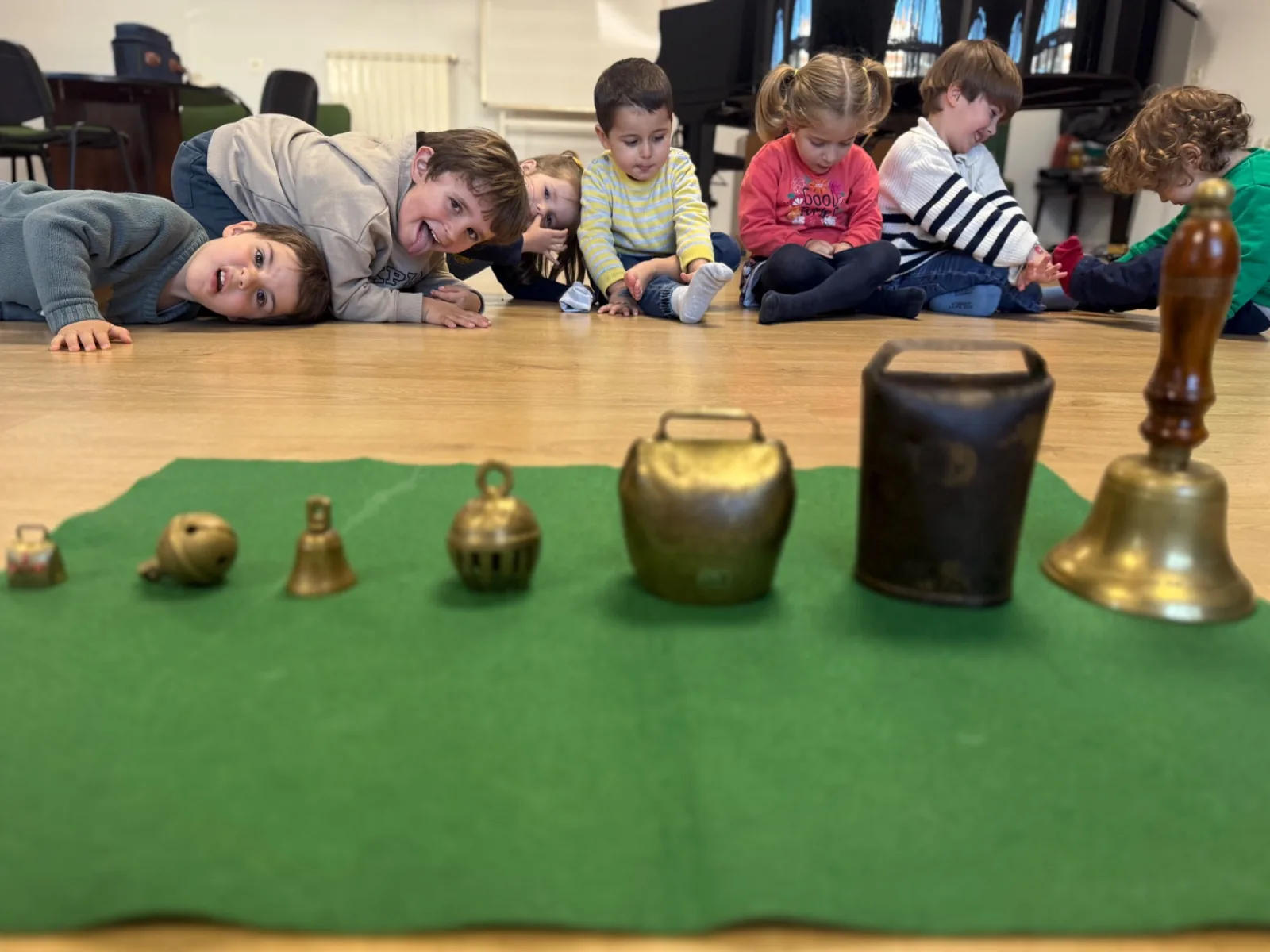 Niños tumbados en el suelo ante una fila de campanas de distintos tamaños
