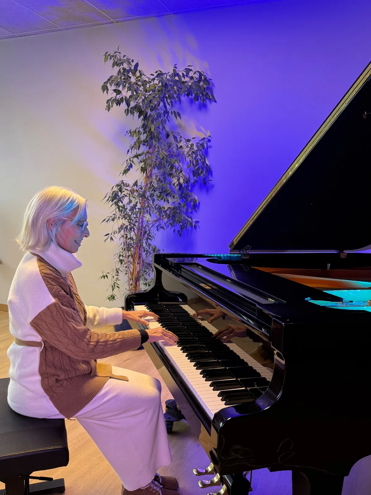 Mujer tocando un piano de cola en un aula con luz azul