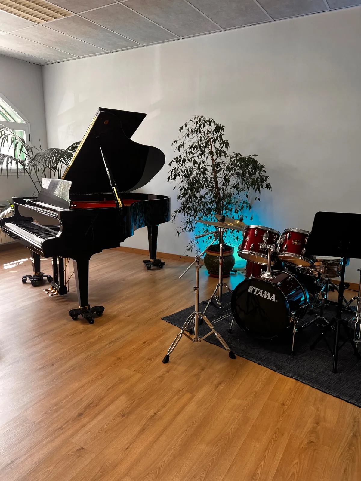 Aula luminosa con piano de cola y batería con atril