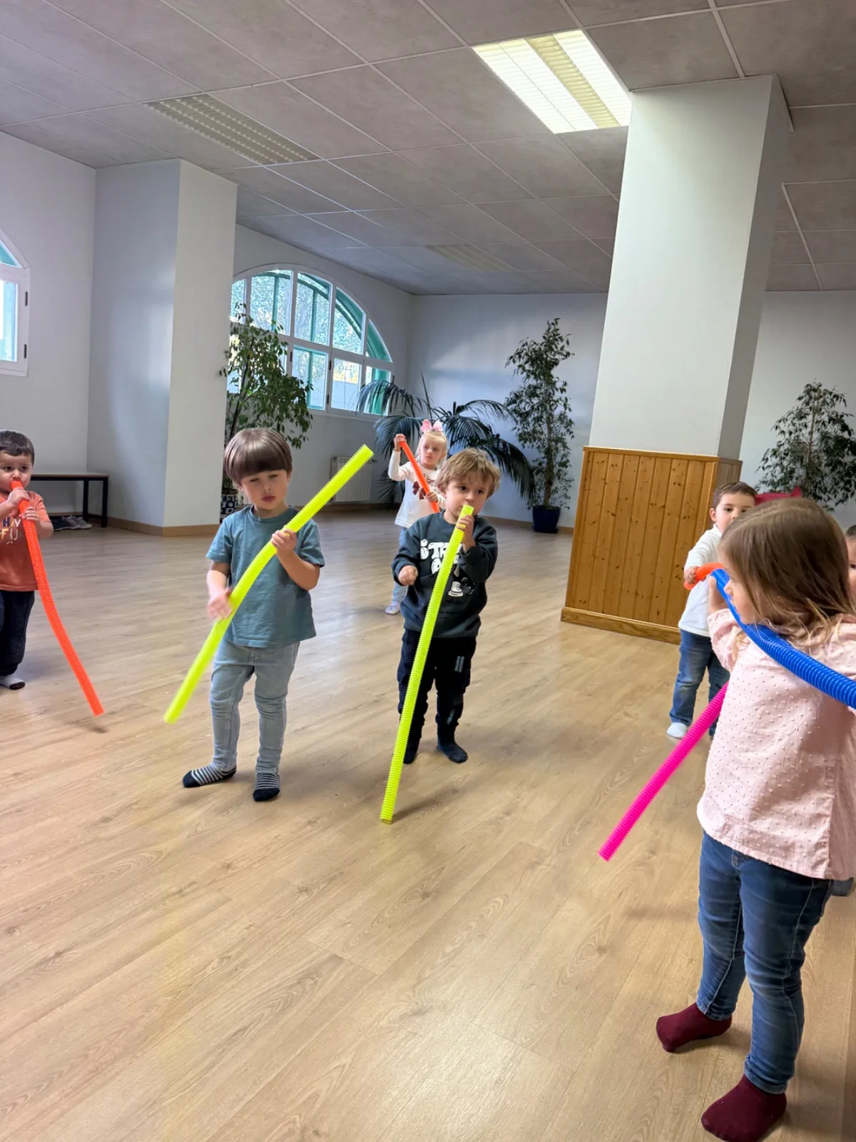 Niños con tubos de colores en una actividad de movimiento en un aula amplia